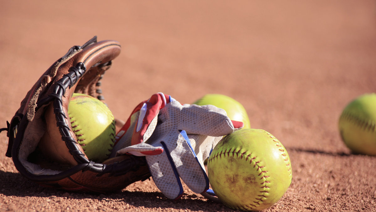 Softball glove and yellow softballs on the field