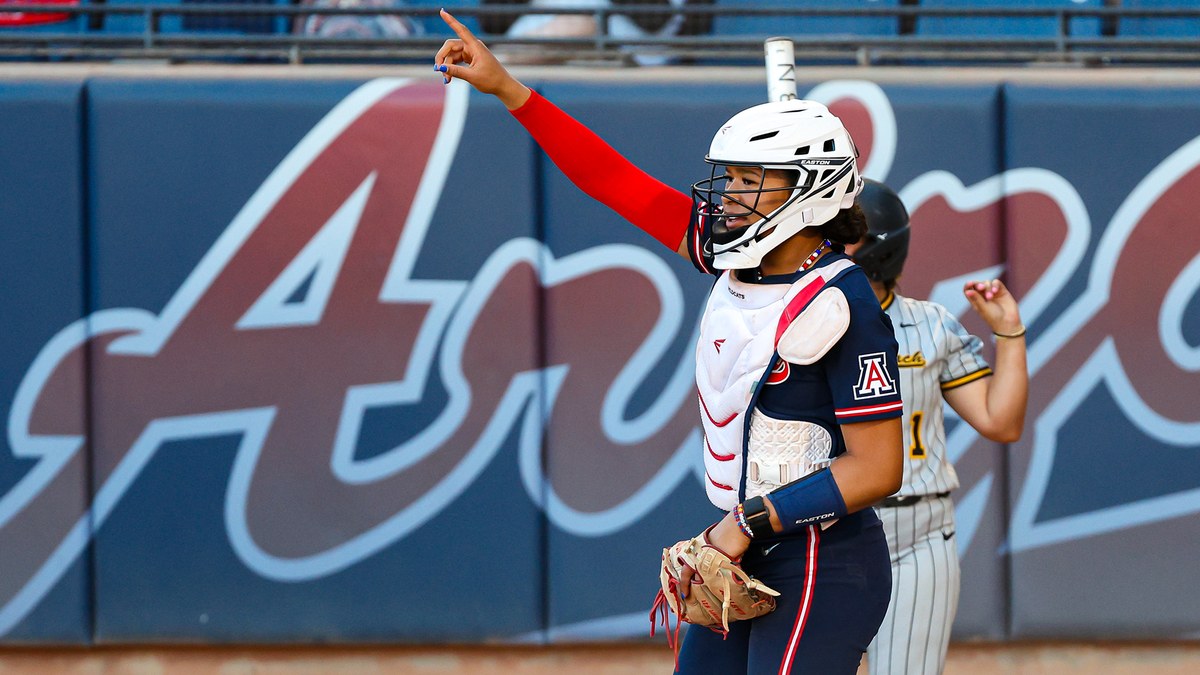 Arizona catcher Sydney Stewart points toward the dugout in catcher's gear